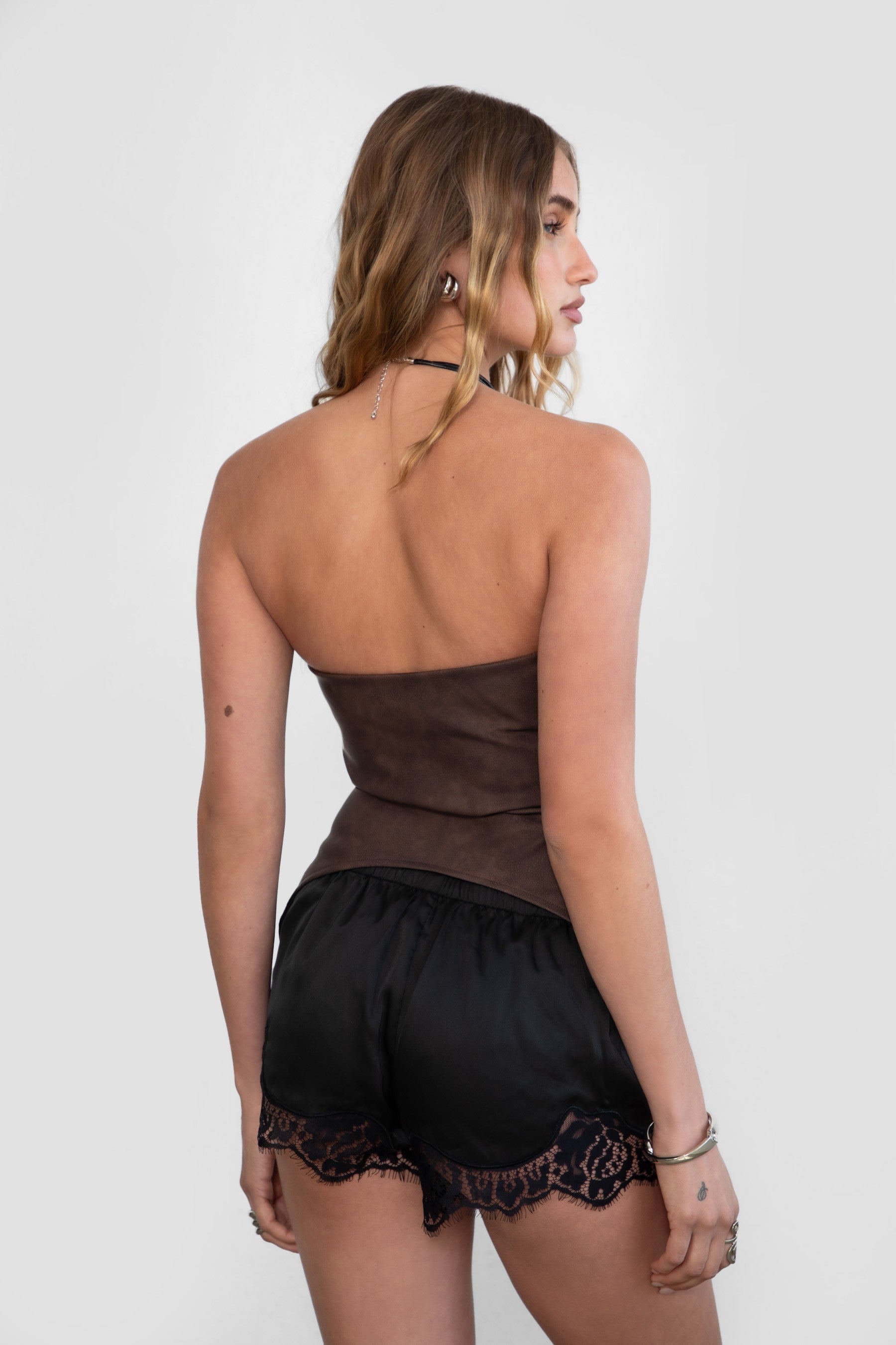 TIC TOC TC30946 RHIANNA PU Vegan Leather Strapless Top in brown. Features a sweetheart neckline, open torso with lace-up detail, structured corset fit, and asymmetrical curved hem.