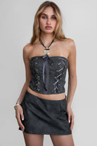 TIC TOC TH30496 ANGIE Distressed PU Corset Top. A strapless leather-look corset with lace-up details, exposed seams, and a satin bow accent.