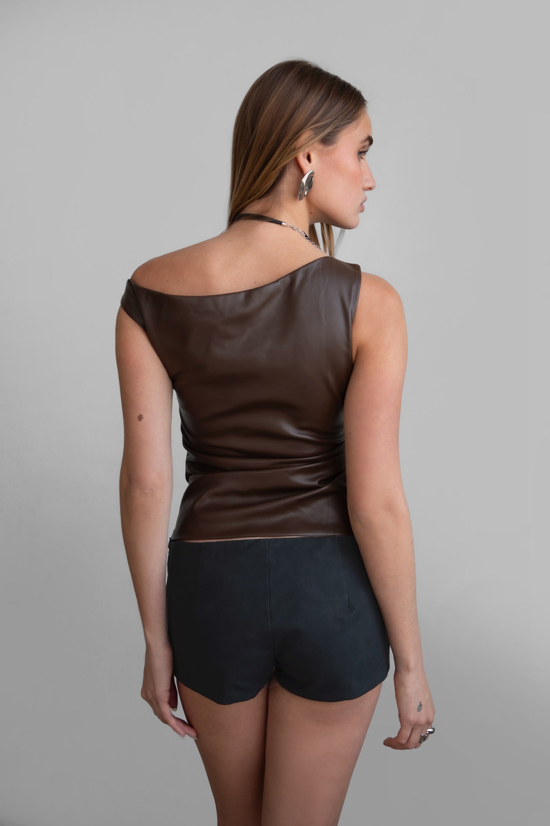 TIC TOC TH30973 SHOCO PU Vegan Leather Top in sleek vegan leather. Features a single off-the-shoulder design, ruched bodice, and hidden zipper closure.